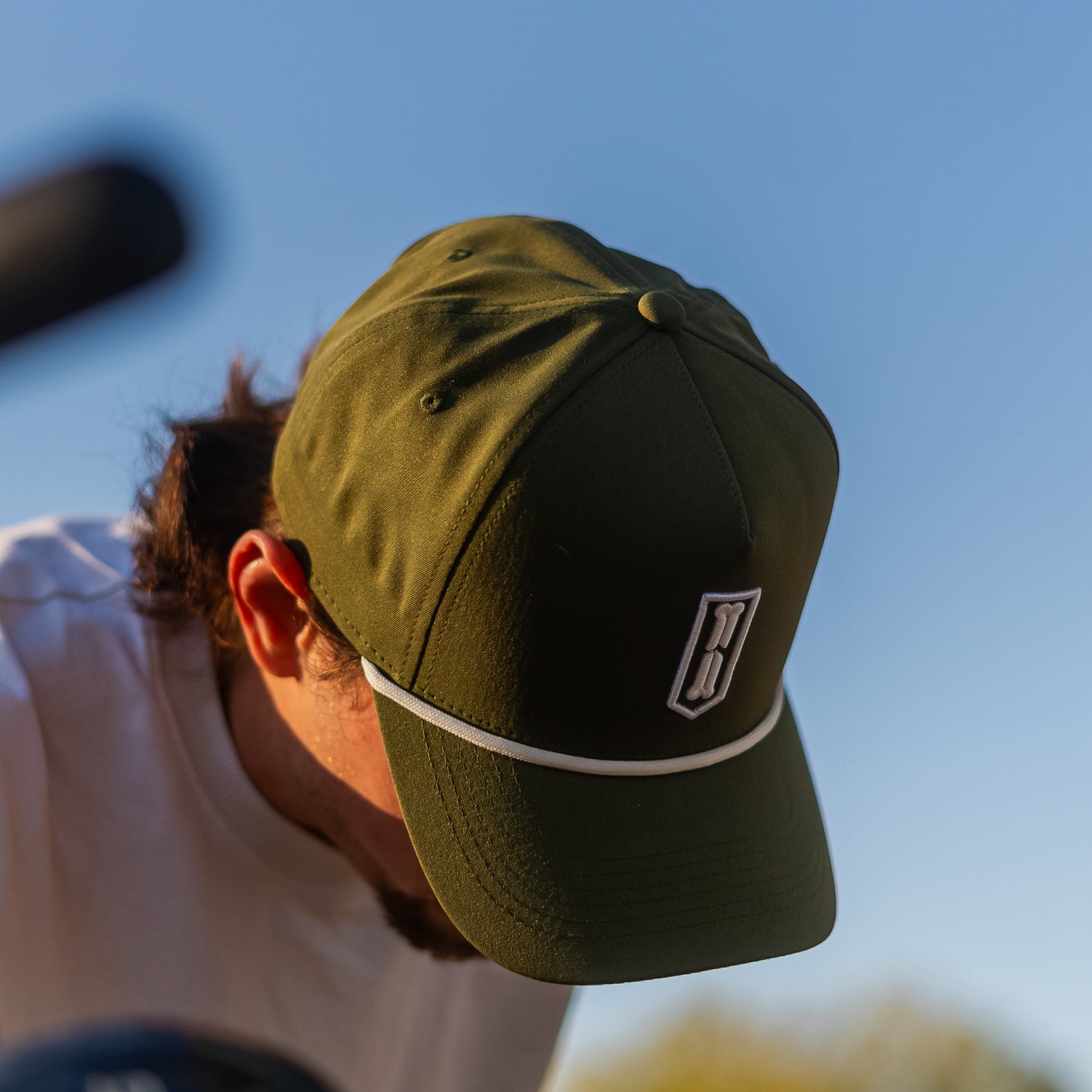 Person wearing a green golf hat with a logo against a blue sky