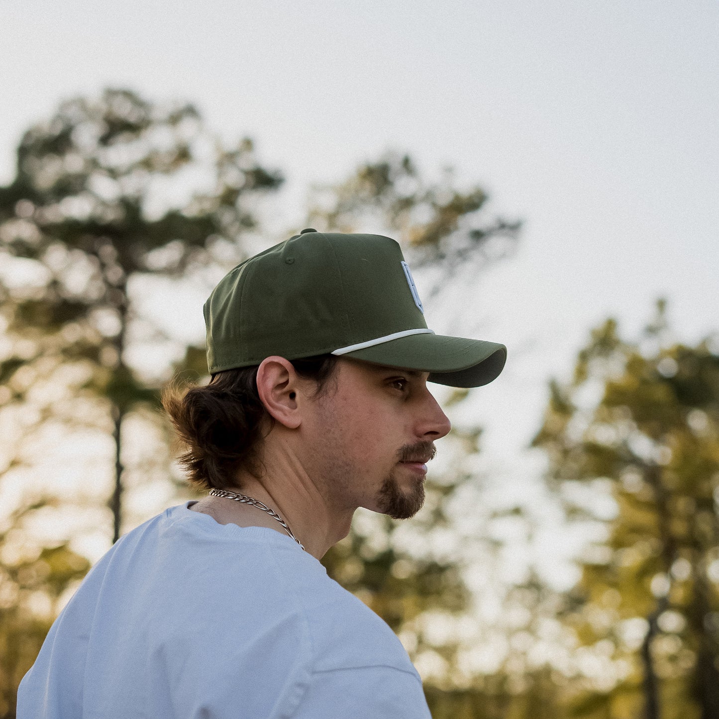 Man wearing a green cap and light blue shirt with trees in the background