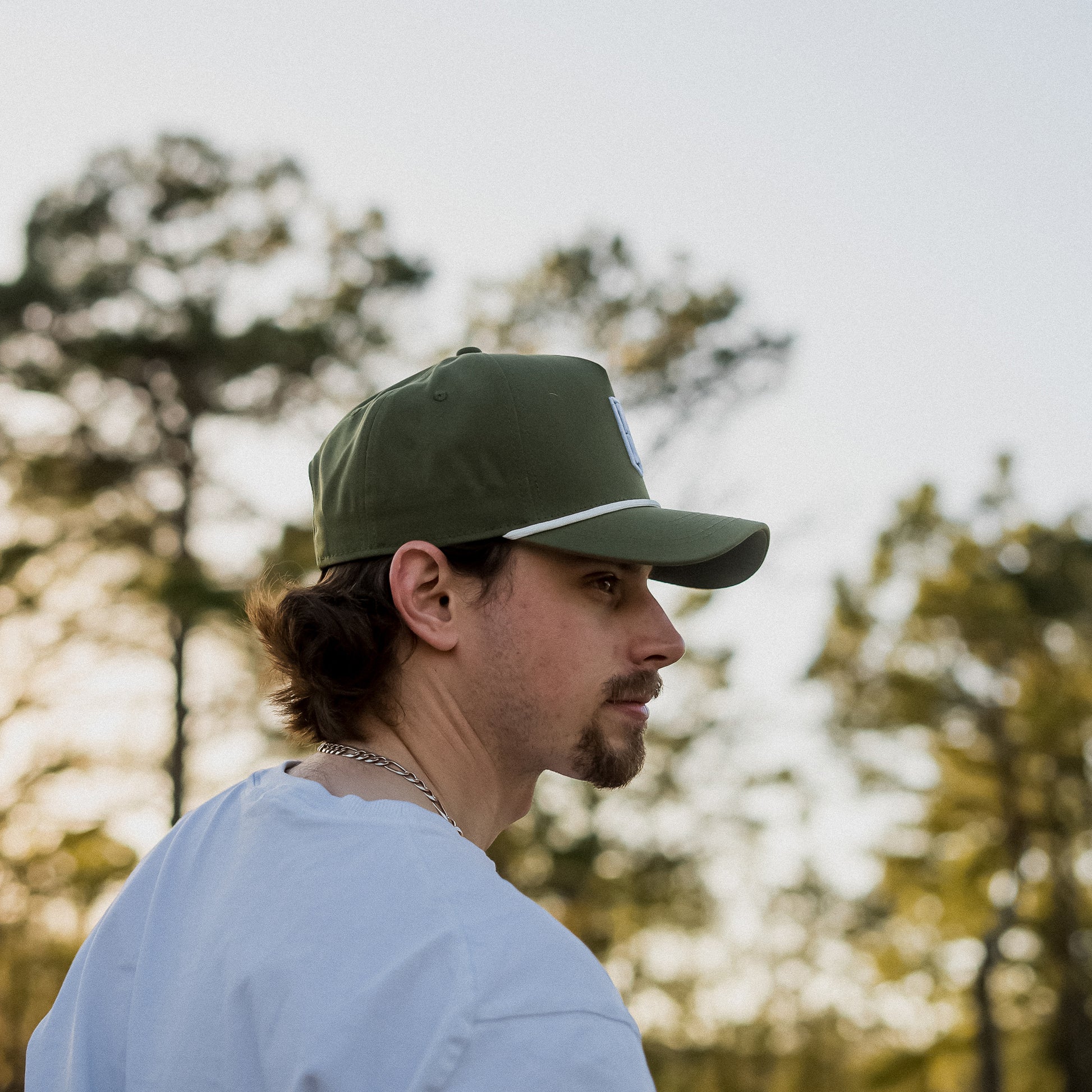 Man wearing a green cap and light blue shirt with trees in the background